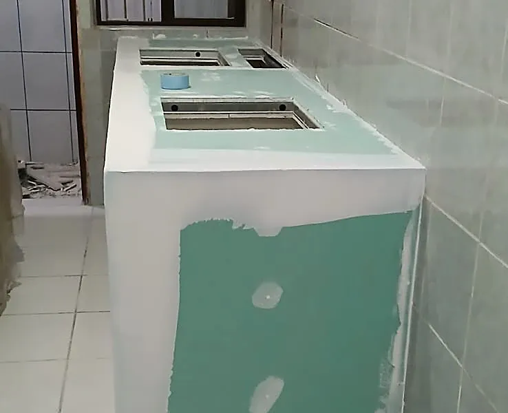 Bancada em drywall antes e depois: à esquerda em montagem, com a placa verde resistente à umidade; à direita pronta, com acabamento branco