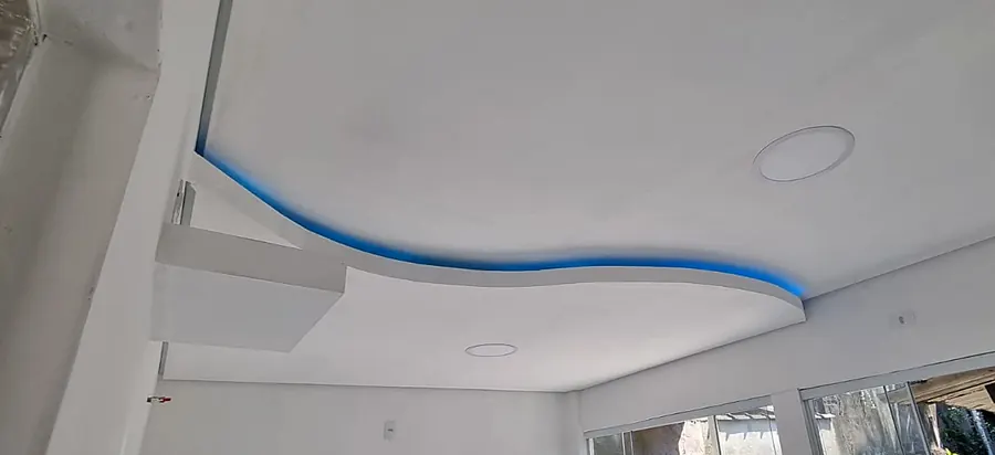 Forro rebaixado em gesso drywall com sanca curva iluminada por fita de LED azul e plafons embutidos
